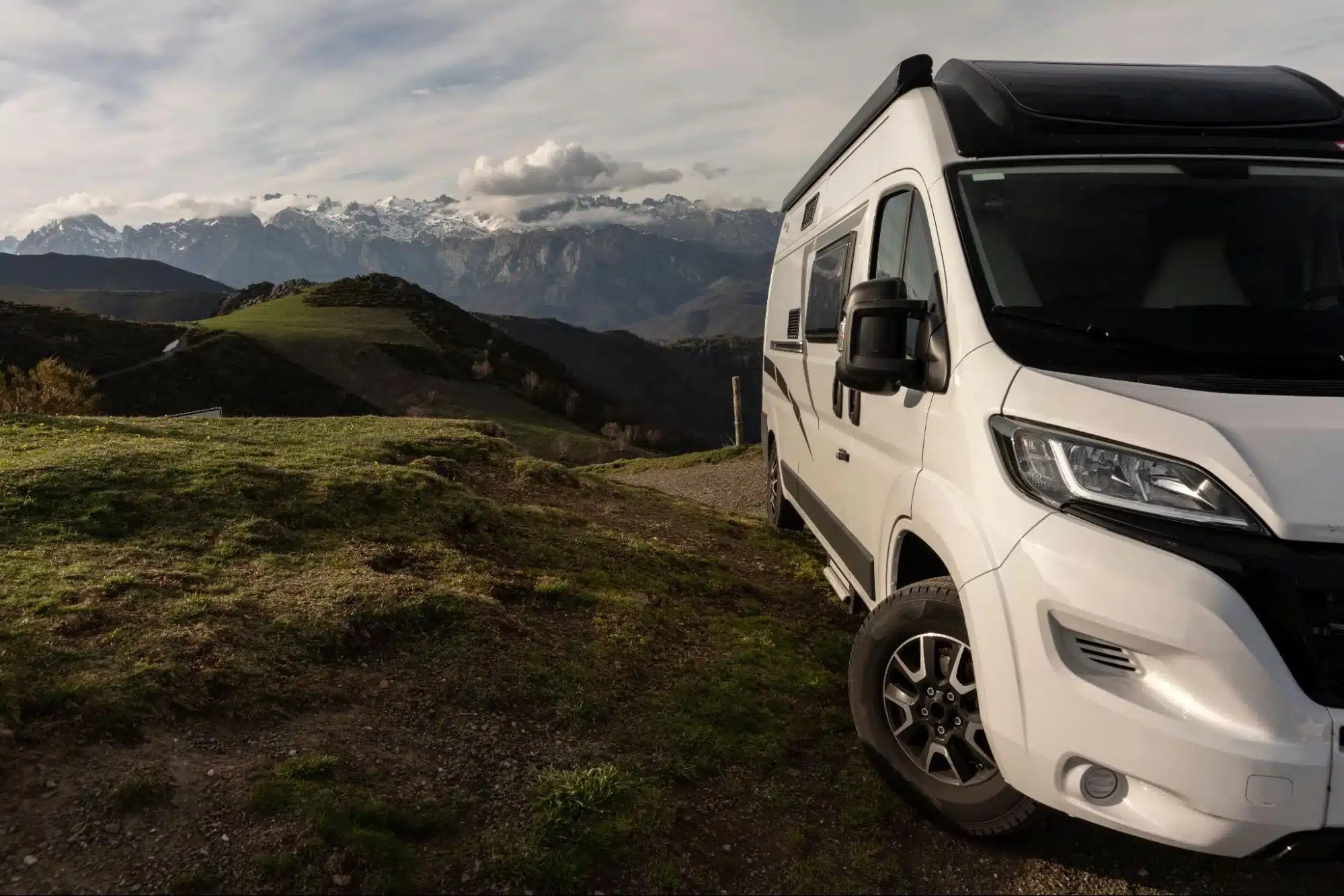 Camper van parked on a scenic hillside with mountains in the background.