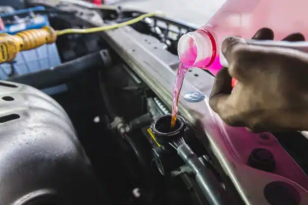 Understanding the role of antifreeze and coolant in cold weather in Durango, CO with Firestone of Durango. Image of mechanic hand pouring pink antifreeze into the coolant reservoir in a car radiator.