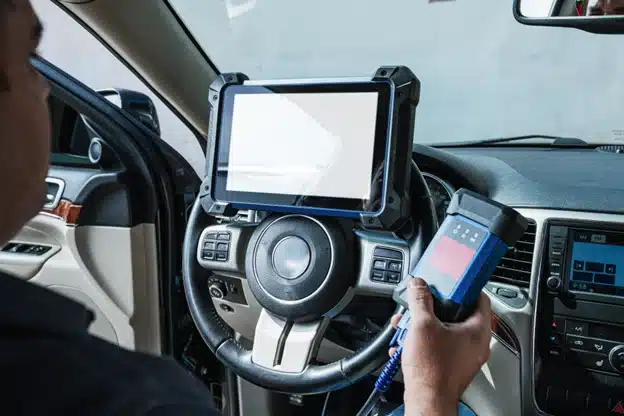 Full vehicle inspection in Durango, CO with Firestone of Durango. Image of mechanic using a digital inspection tool on the steering wheel of a car in the shop holding a tester to perform a full inspection while in the shop.