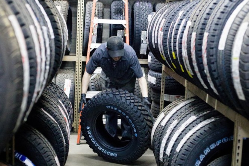 New Tires in Durango CO At Firestone of Durango. Mechanic holding new tires in a tire shop with tires displayed in the background