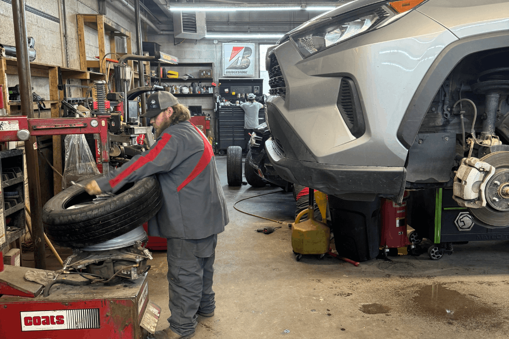 Summer car prep, auto repair in Durango, CO, at Firestone of Durango. Image of a technician mounting and balancing a tire while a vehicle is serviced in the shop, highlighting professional tire replacement, wheel balancing, brake inspections, and routine automotive maintenance for safe driving.