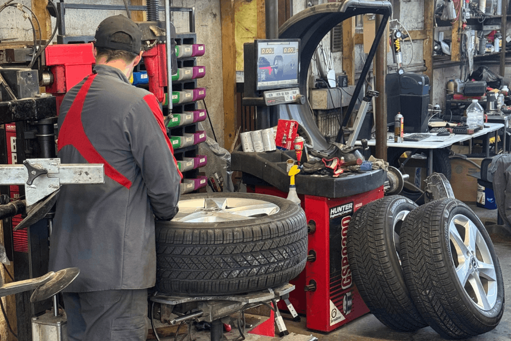 AWD tire replacement, auto repair in Durango, CO at Firestone of Durango. Image of a technician working at a tire balancing machine with several mounted tires nearby for maintenance and service.