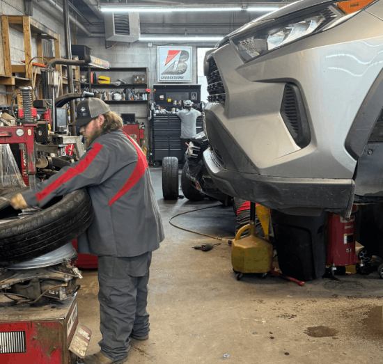 Summer car prep, auto repair in Durango, CO, at Firestone of Durango. Image of a technician mounting and balancing a tire while a vehicle is serviced in the shop, highlighting professional tire replacement, wheel balancing, brake inspections, and routine automotive maintenance for safe driving.