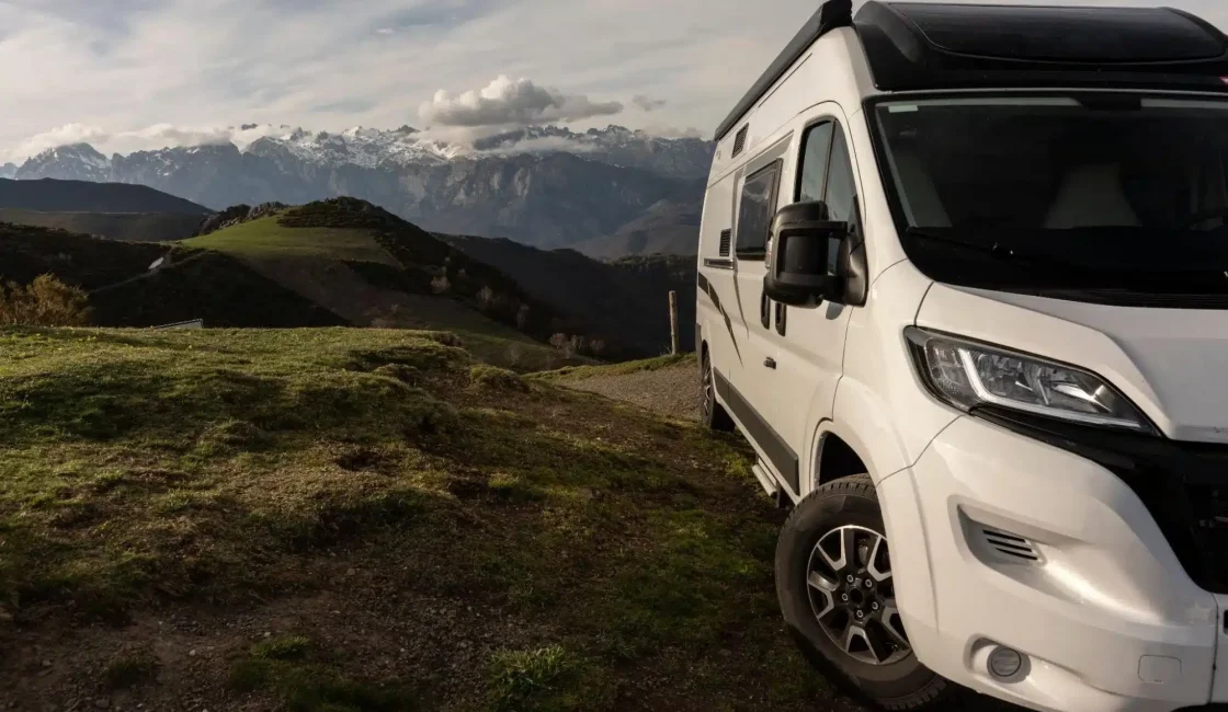 Camper van parked on a scenic hillside with mountains in the background.